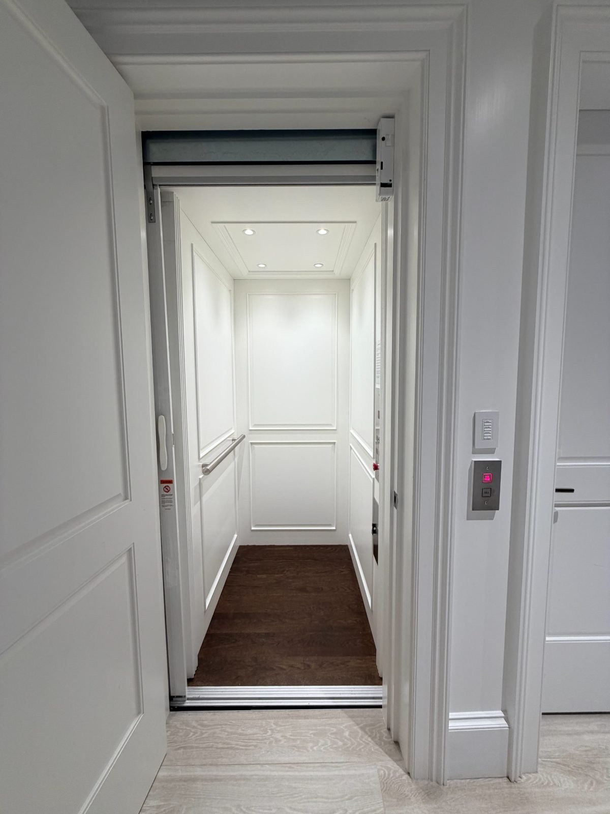 White panelled residential elevator cab with dark hardwood floor